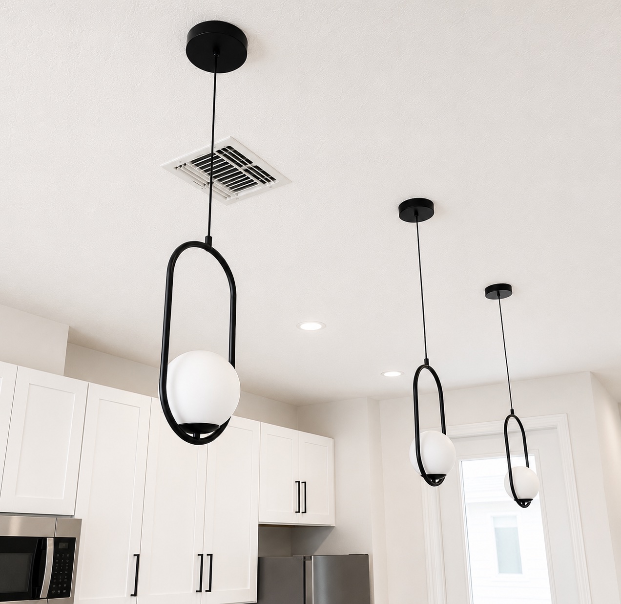 Modern black pendant lights installed over a white kitchen with stainless steel appliances